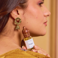 A small clear glass bottle with wooden cap and dropper containing golden-yellow mogra attar by rooh handcrafted in Kannauj