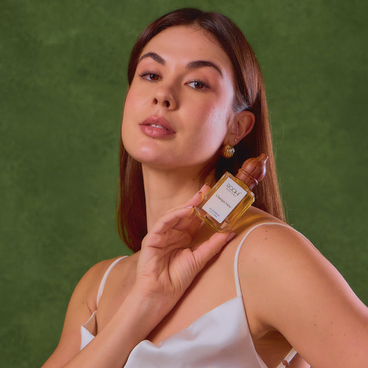 A clear glass bottle with a golden cap and white label containing amber-colored champa muse eau de parfum