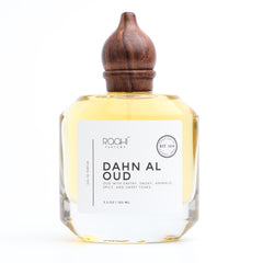 A clear glass bottle with a dark brown wooden stopper containing golden-yellow dahn al oud eau de parfum by roohi parfums