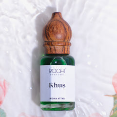 A small green glass bottle with wooden cap labeled raaahi parfums khus indian attar handcrafted in kannauj