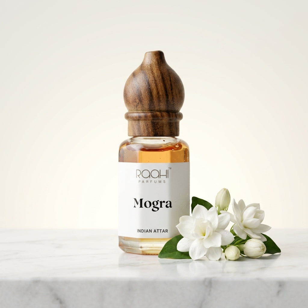 A clear glass bottle with a dark wood cap labeled mogra indian attar by roahi parfums handcrafted in kannauj