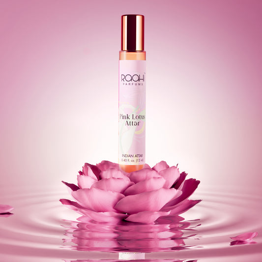 A slender transparent glass bottle with rose gold cap and label containing amber pink lotus attar by raah parfums 12ml