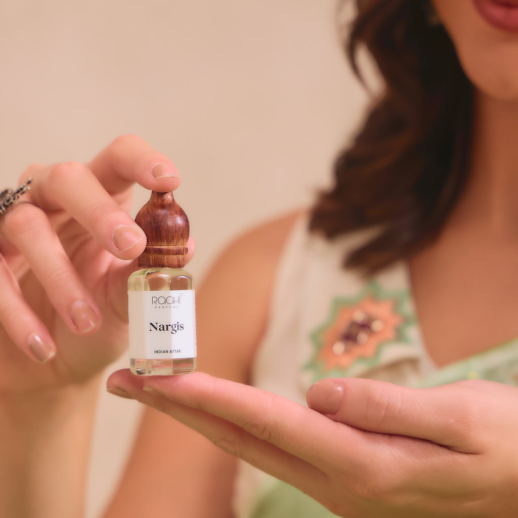 A small clear glass bottle with wooden cap and white label holding roch parfum nargis indian attar fragrance