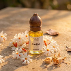 A small clear glass bottle with a dark brown wooden cap contains golden-yellow parijat attar perfume from roahi parfums