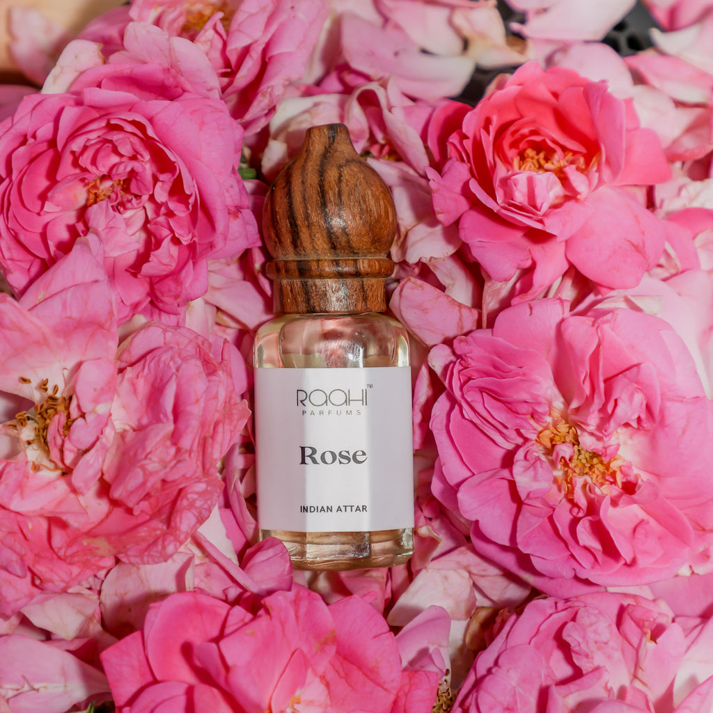 A clear glass bottle with a wooden cap labeled rose indian attar by Roahi Parfums for authentic gulab attar use