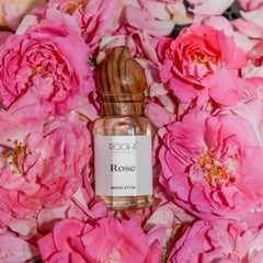 A clear glass bottle with a wooden cap labeled rose indian attar by Roahi Parfums for authentic gulab attar use