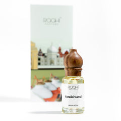 A clear glass bottle with wooden stopper labeled sandalwood indian attar by roohi parfums handcrafted in Kannauj