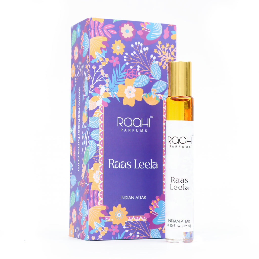 A slender transparent glass rollerball bottle with gold cap and white label containing amber indian attar perfume from raahi parfums raas leela 12ml