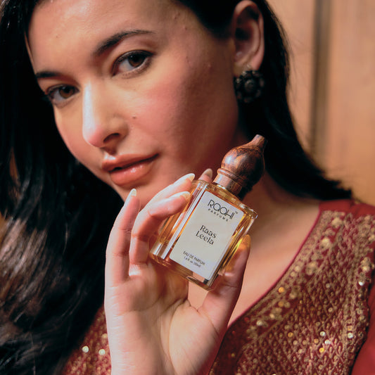 A clear glass bottle of roohi parfums raas leela eau de parfum with gold liquid and wooden stopper 50ml