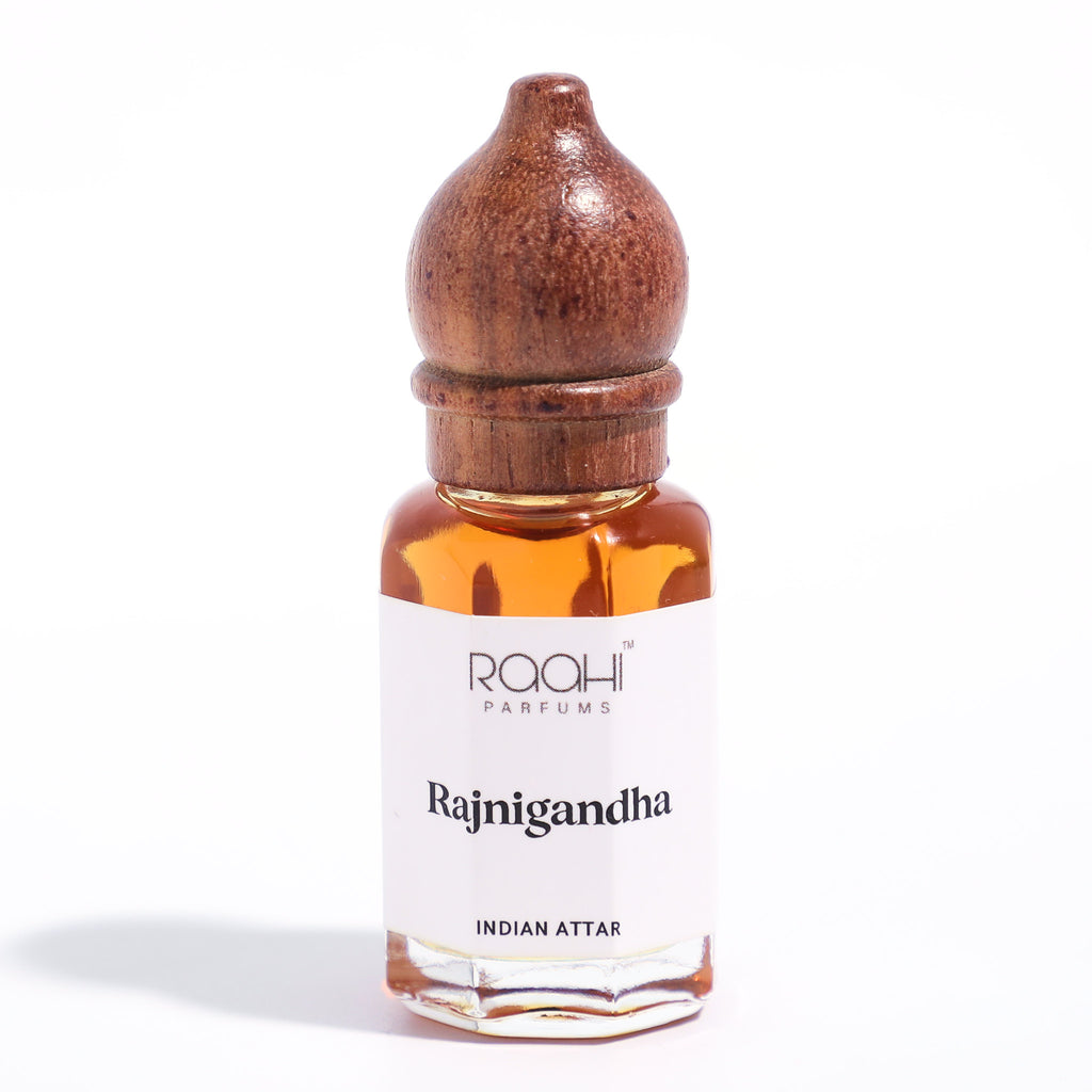 A small glass bottle of rajnigandha tuberose attar with rich amber liquid and ornate dark brown wooden stopper from raahi parfums
