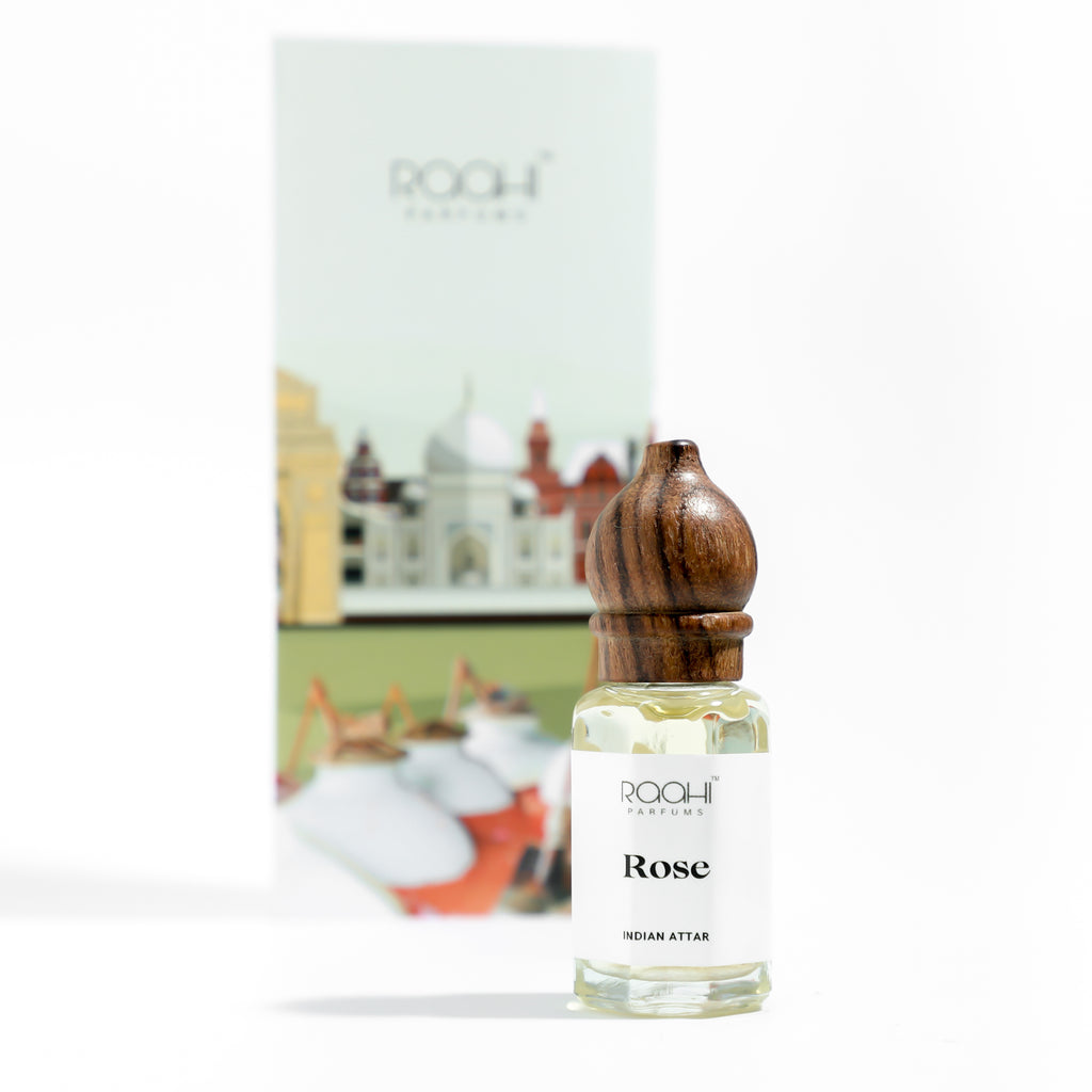 A clear glass bottle with wooden cap labeled rose indian attar by rqah parfums for authentic gulab attar use