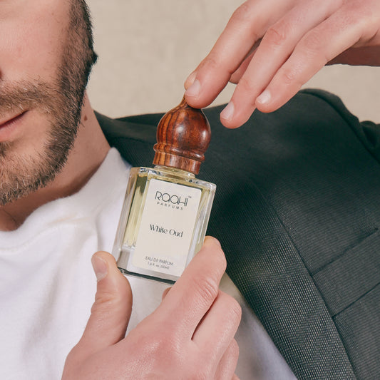 A clear glass bottle of raahi parfums white oud eau de parfum 50ml with polished wooden cap and minimalist white label