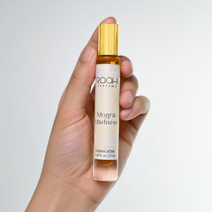 A sleek transparent glass rollerball bottle with gold cap and cream label holding Raahi Parfums mogra madness Indian attar 12ml