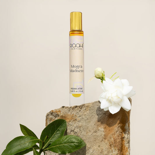 A sleek transparent glass rollerball bottle of raahi parfums mogra madness indian attar with a gold cap and label
