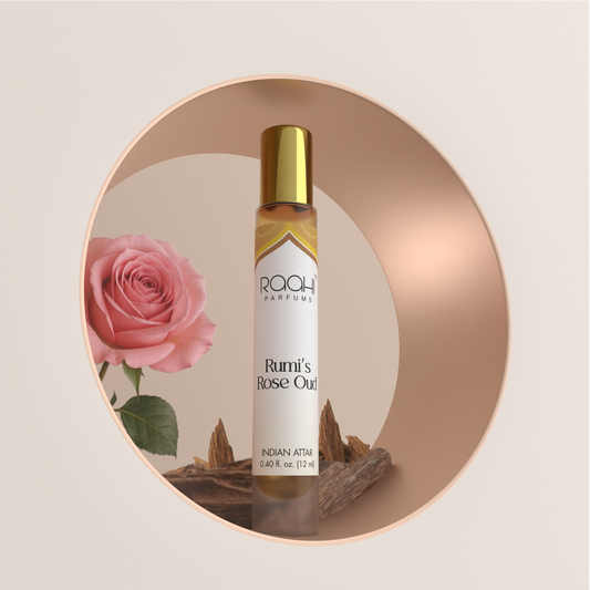 A slender transparent glass rollerball bottle with gold cap and white label containing amber indian attar rumi’s rose oud by roahi parfums